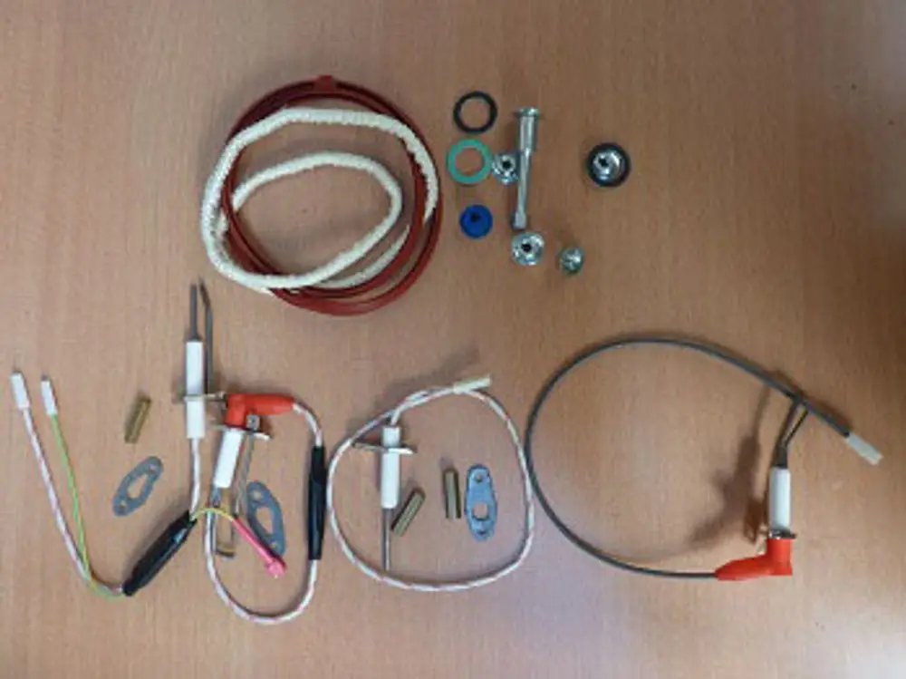 Remeha Wartungssatz mit verschiedenen Komponenten, darunter Kabel, Stecker, Unterlegscheiben und andere Bauteile, die auf einer Holzoberfläche angeordnet sind.